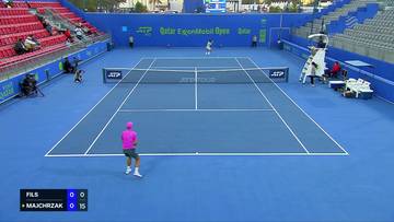 Gracz tenisa w różowej czapce i koszulce na niebieskim korcie, przygotowuje się do zagrania.