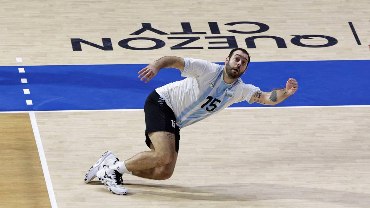 Siatkarz w białej koszulce z numerem 15 i czarnych spodenkach, pochylony na boisku siatkarskim. Na tle widoczny napis QUEZON CITY.