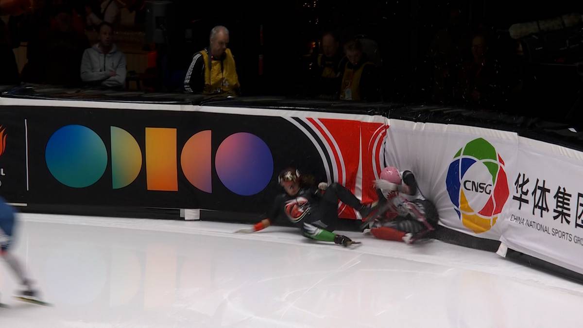 Dwóch zawodników z polskiej sztafety upadło na lodowisku podczas zawodów panczenowych. Jeden z nich leży na plecach, drugi na boku, obaj w kombinezonach sportowych. W tle widoczni są inni panczeniści oraz fragmenty band reklamowych z logotypami.