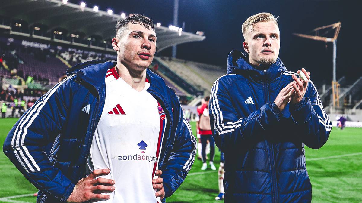 Dw&oacute;ch piłkarzy na boisku piłkarskim nocą, w tle widać oświetlone trybuny stadionu.