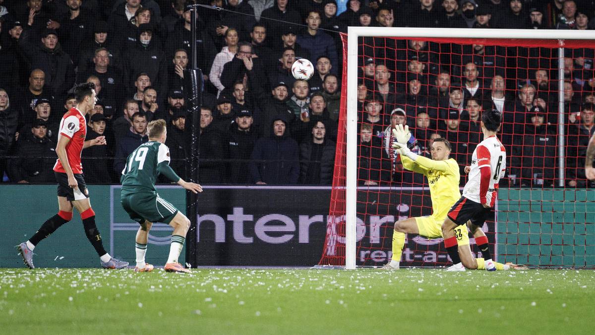 Mecz piłki nożnej, bramkarz w żółtym stroju broni strzał zawodnika w zielonym stroju.