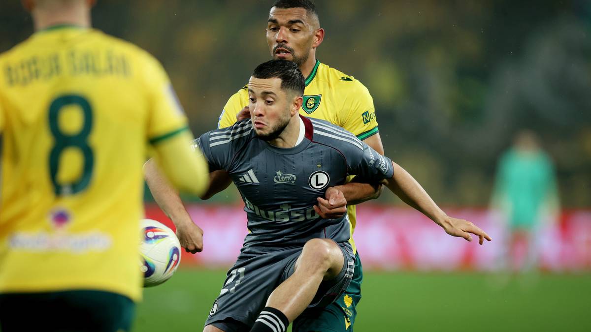 Piłkarz w szarym stroju walczy o piłkę z zawodnikiem w ż&oacute;łtym stroju.