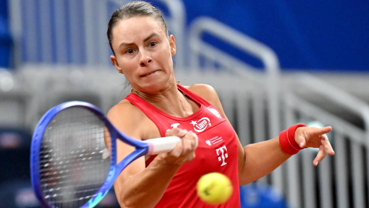 Kobieta podczas meczu tenisowego, w czerwonym stroju sportowym, uderza rakietą piłkę tenisową.