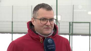 Mężczyzna w okularach i czerwonej kurtce z kapturem trzyma mikrofon Polsat Sport.