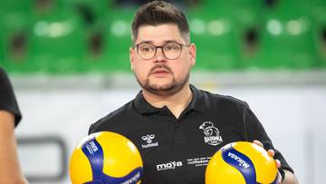 Mężczyzna w okularach i czarnej koszulce z logo klubu trzyma dwie ż&oacute;łto-niebieskie piłki do siatk&oacute;wki.