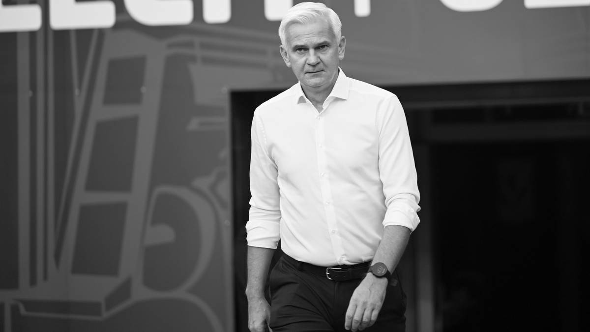 Starszy mężczyzna w białej koszuli i ciemnych spodniach idący w stronę kamery.