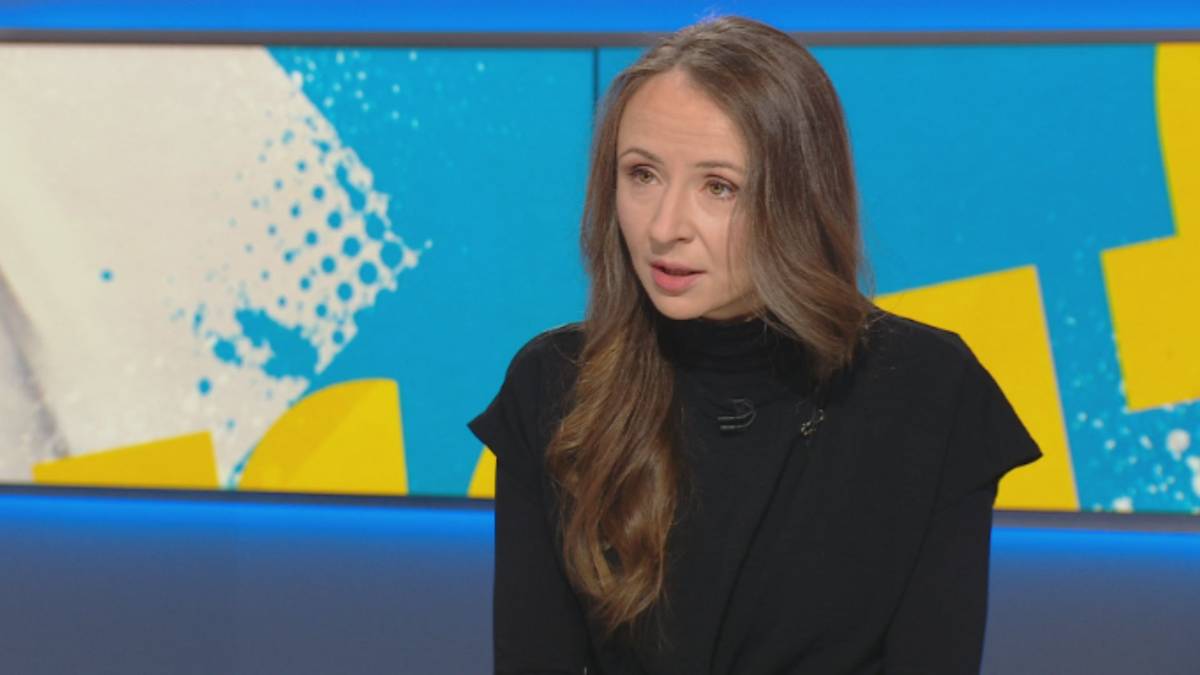 Kobieta w czarnej sukience z golfem siedzi na tle niebiesko-ż&oacute;łtego ekranu.