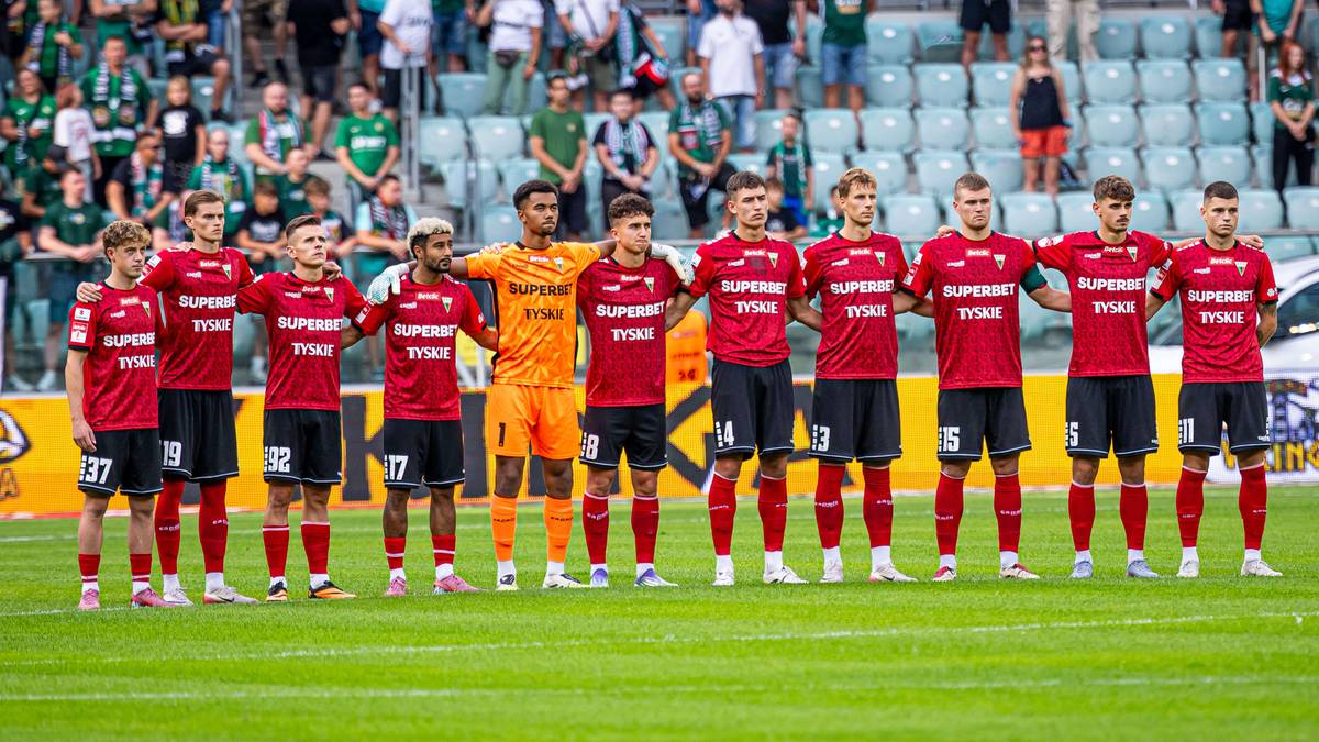 Drużyna piłkarska w czerwonych strojach ustawiona w rzędzie na boisku.