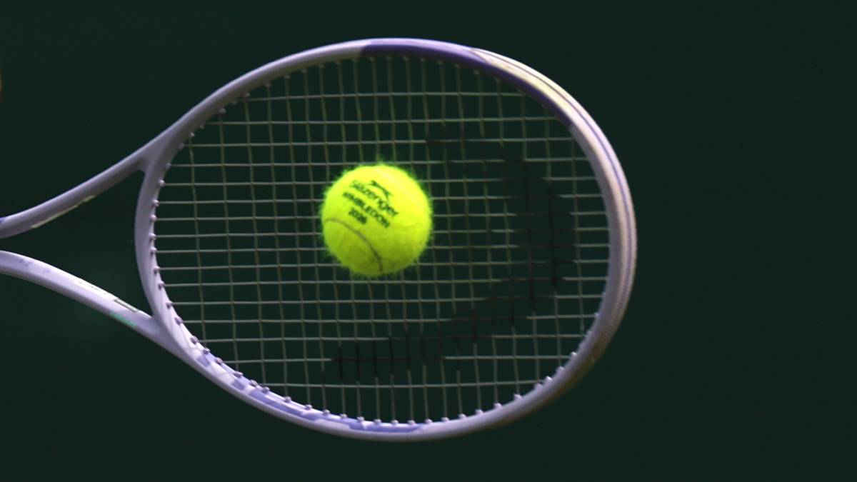 Kobieta grająca w tenisa, uderza piłkę rakietą w biały str&oacute;j sportowy.