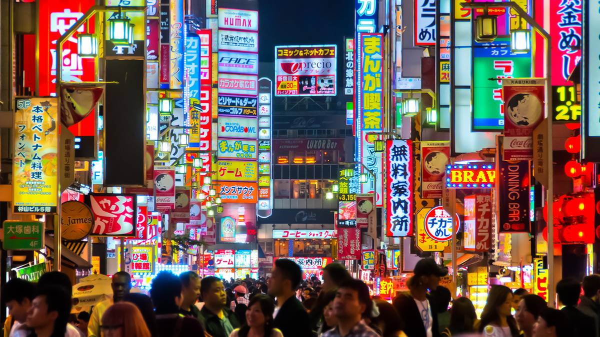 Zatłoczona nocna ulica w Japonii, pełna kolorowych neon&oacute;w i szyld&oacute;w reklamowych oraz przechodni&oacute;w na pierwszym planie.