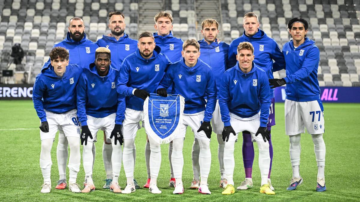 Drużyna piłkarska Lecha Poznań w komplecie, stojąca na boisku w niebieskich strojach.