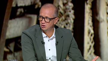 Mężczyzna w okularach i marynarce, m&oacute;wiący w studio.
