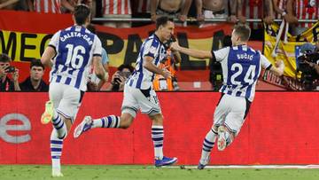 Trzech piłkarzy w białych strojach z niebieskimi pasami świętuje bramkę.