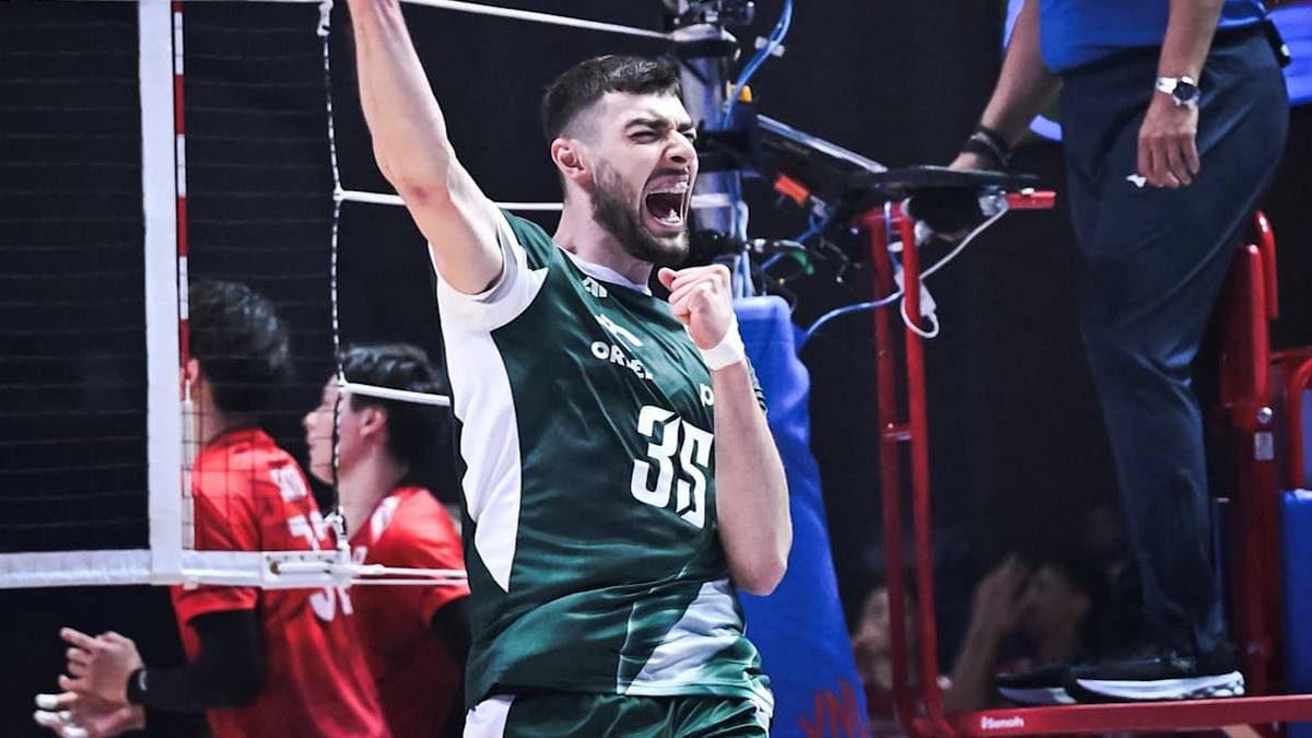 Zawodnik siatkówki w zielonej koszulce z numerem 35 krzyczy z radości, unosząc prawą rękę z zaciśniętą pięścią. W tle widoczni są inni zawodnicy oraz siatka.