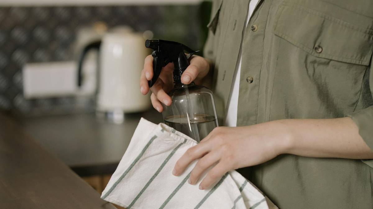 Osoba trzyma butelkę z rozpylaczem i ściereczkę, przygotowując się do sprzątania.