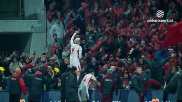 Piłkarz w białej koszulce z numerem 9 świętuje z kibicami na trybunach, kt&oacute;rzy są ubrani w czerwone barwy i machają rękami.
