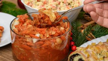 Dłoń trzymająca łyżkę z potrawą z marchewki i innych warzyw, na tle świątecznych dekoracji i innych potraw.