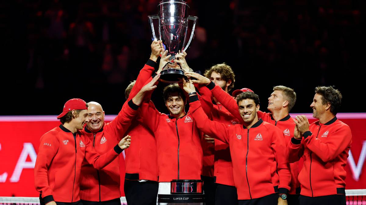 Drużyna tenisist&oacute;w w czerwonych strojach świętuje zwycięstwo, trzymając w g&oacute;rze puchar.