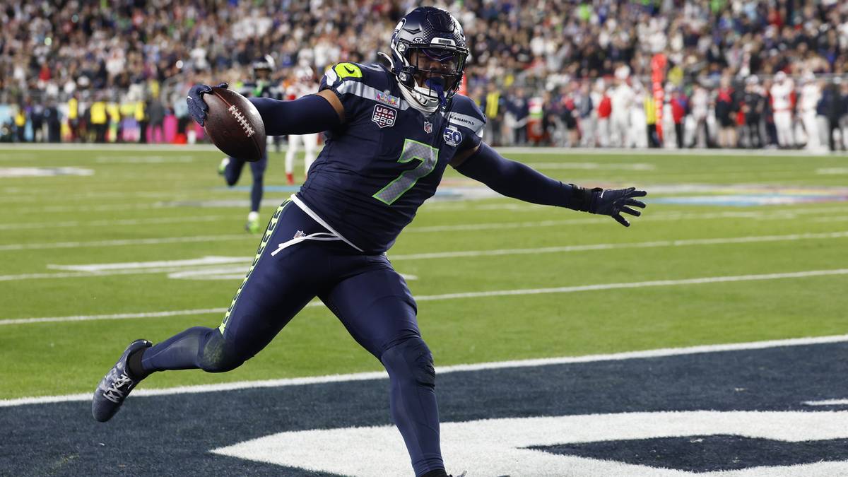 Gracz futbolu amerykańskiego w ciemnoniebieskim stroju biegnie z piłką w kierunku strefy punktowej.