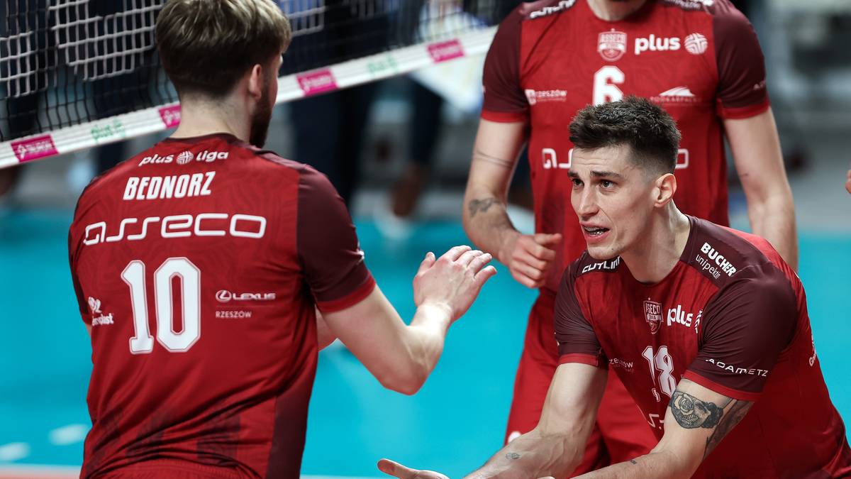 Dw&oacute;ch siatkarzy w czerwonych koszulkach z numerami 10 i 18, gestykulujący do siebie na boisku do siatk&oacute;wki.