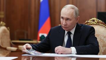 Mężczyzna w garniturze siedzi przy stole, trzymając dokumenty.