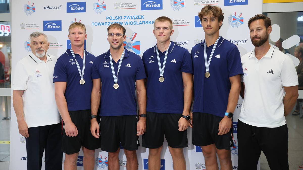 Pięciu młodych mężczyzn w strojach sportowych i dwóch starszych mężczyzn w koszulach stoi na tle ściany z logotypami.