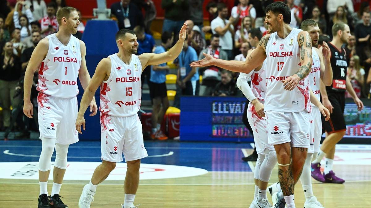 Koszykarze w białych strojach reprezentacji Polski "POLSKA" grający w meczu, jeden z zawodników wykonuje gest "piątki" z kolegą z drużyny.
