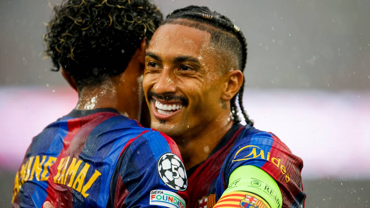 Dw&oacute;ch piłkarzy FC Barcelony przytulających się po udanej akcji na boisku. Jeden z nich, z widoczną opaską kapitańską, uśmiecha się szeroko, podczas gdy drugi, odwr&oacute;cony plecami, r&oacute;wnież wydaje się być w dobrym nastroju.