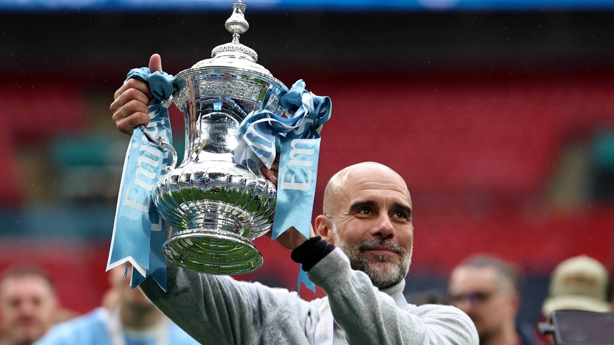 Pep Guardiola trzymający trofeum, z lekkim uśmiechem na twarzy.