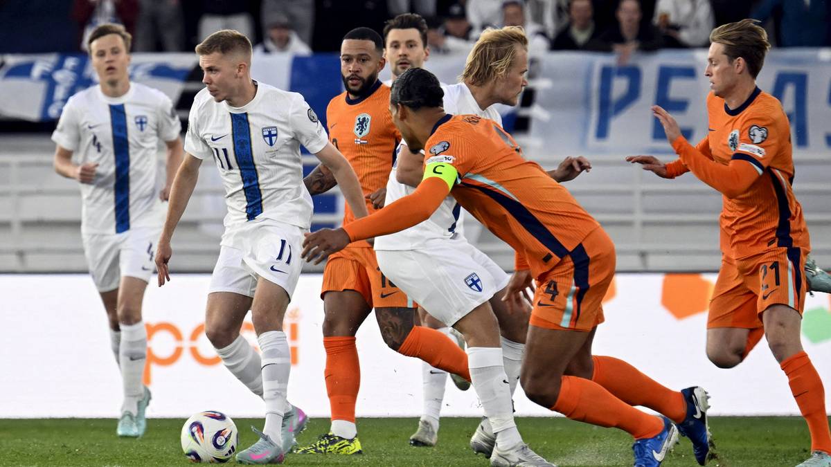 Piłkarze w białych i pomarańczowych strojach rywalizują na boisku podczas meczu piłki nożnej.