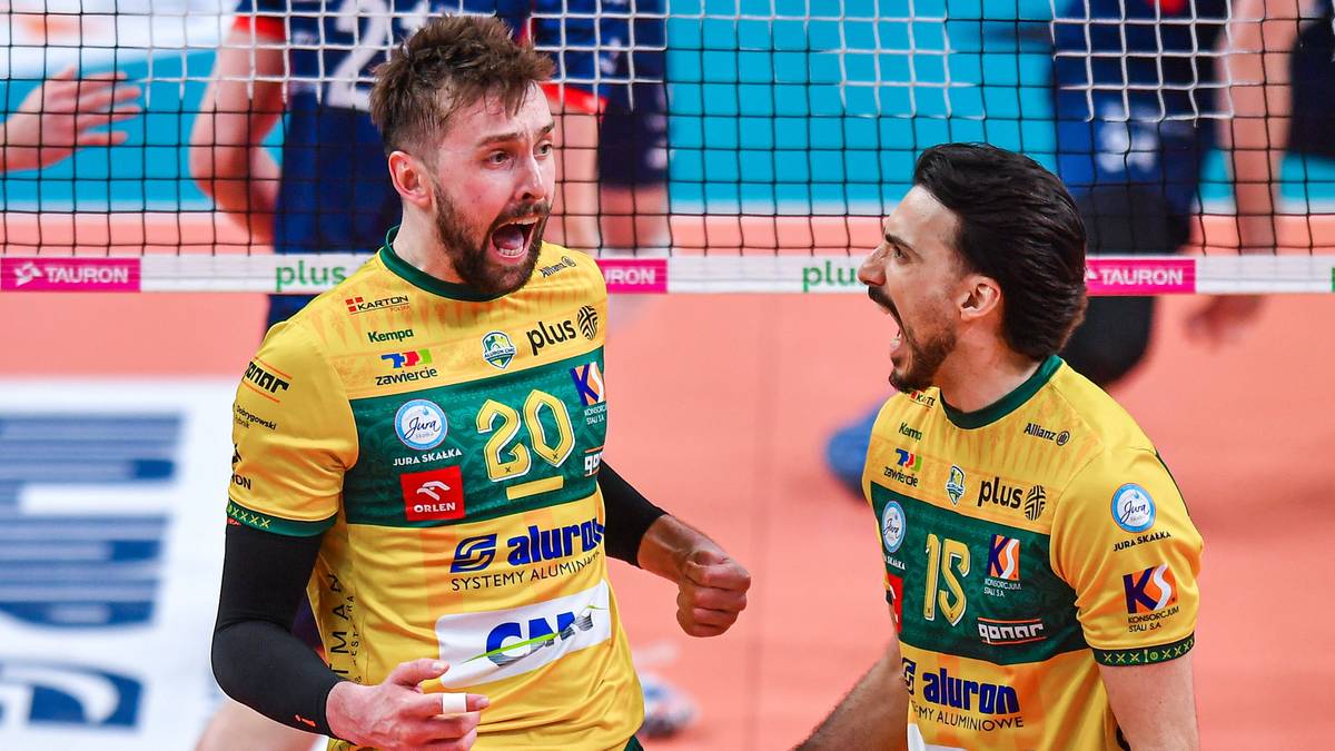 Dw&oacute;ch siatkarzy w ż&oacute;łtych koszulkach z zielonymi akcentami radośnie krzyczy do siebie na tle siatki.