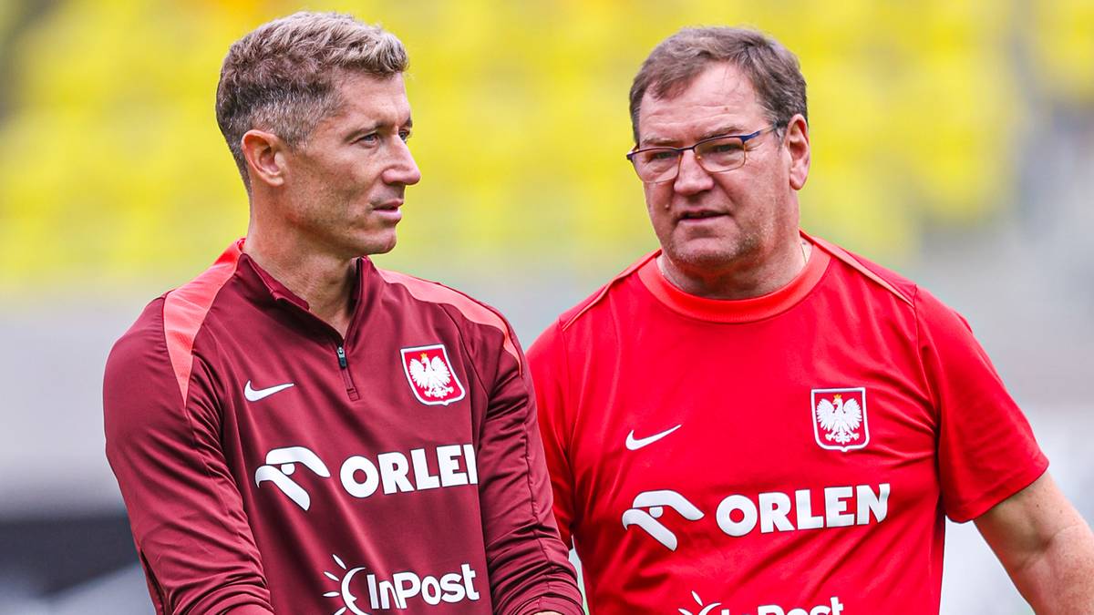 Dw&oacute;ch mężczyzn w strojach reprezentacji Polski, jeden z nich trzyma piłkę, stoją na boisku piłkarskim.