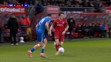 Dw&oacute;ch piłkarzy, jeden w niebieskim stroju, drugi w czerwonym, gra z piłką na boisku piłkarskim.