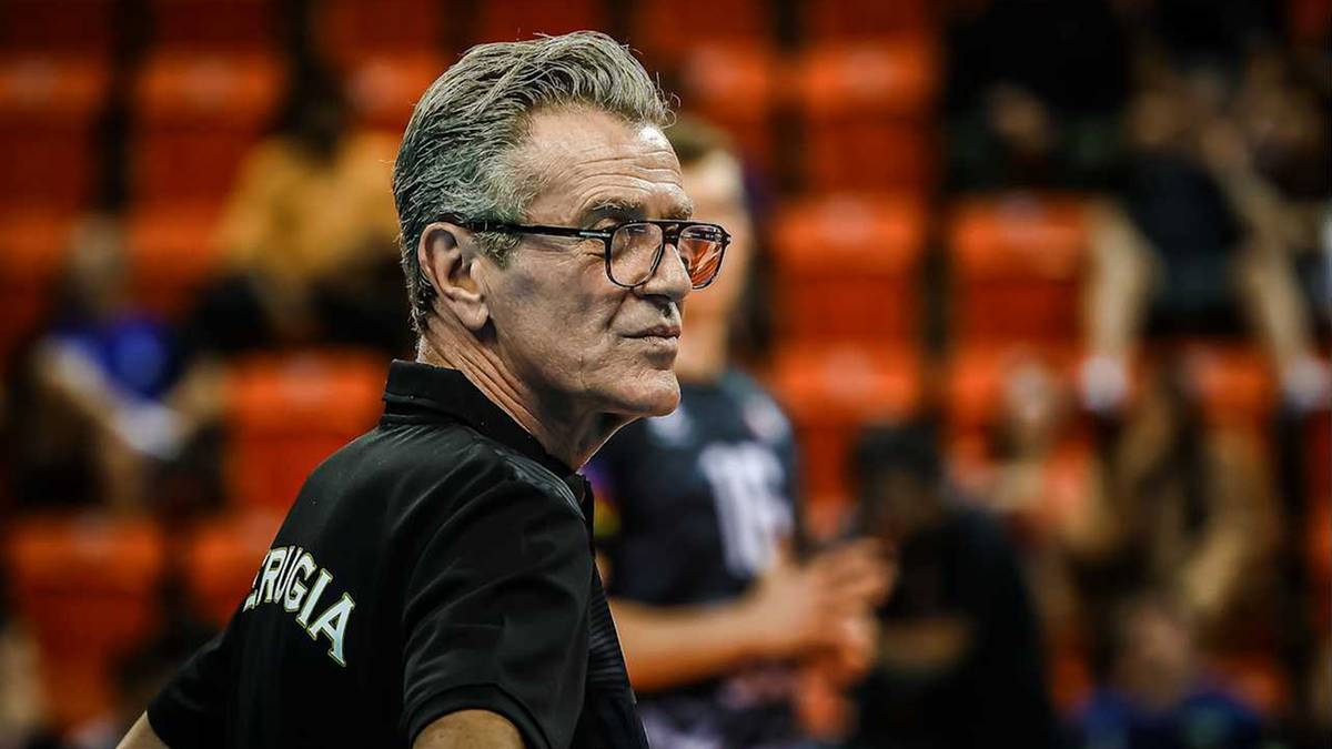 Portret siwego mężczyzny w okularach, ubranego w czarną koszulkę z napisem "PERUGIA", patrzącego w bok.