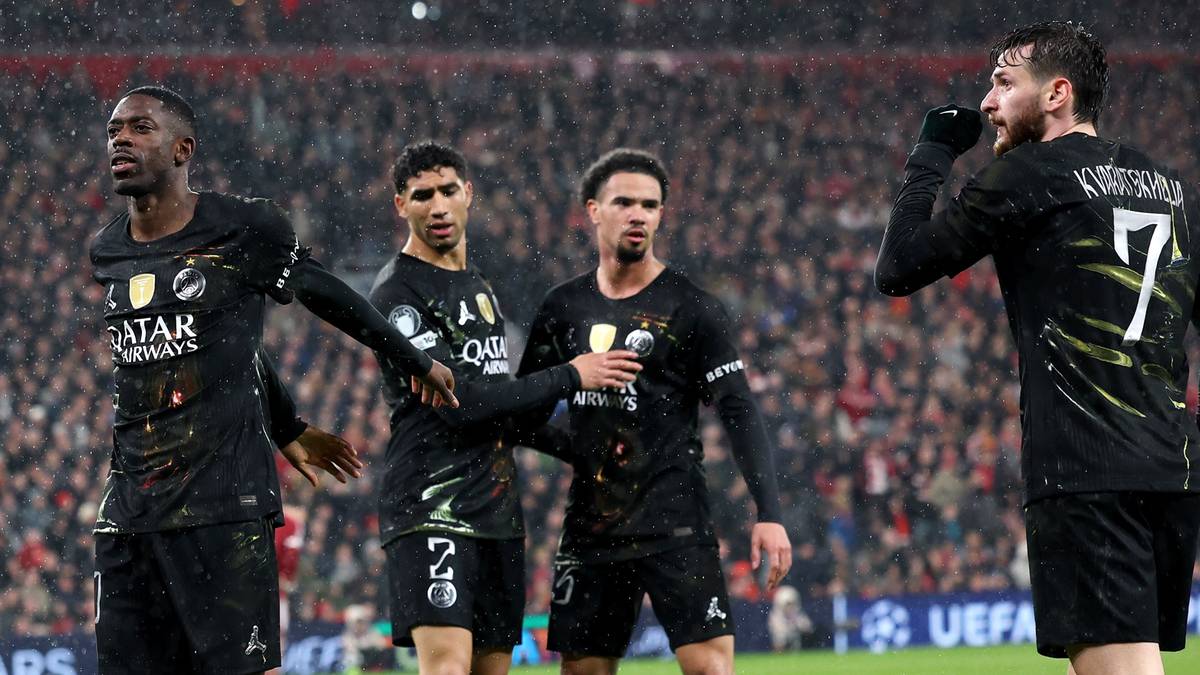 Piłkarze w czarnych strojach na boisku piłkarskim, jeden z nich patrzy w g&oacute;rę.