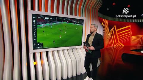 Dariusz Rolak stoi przed dużym ekranem telewizyjnym, na kt&oacute;rym wyświetlany jest obraz meczu piłki nożnej pomiędzy AZ Alkmaar a Jagiellonią Białystok.