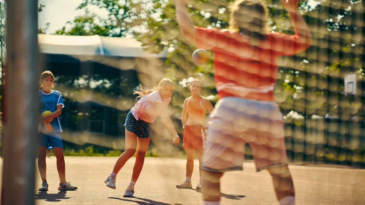 Grupa młodych ludzi grających w piłkę ręczną na boisku zewnętrznym.