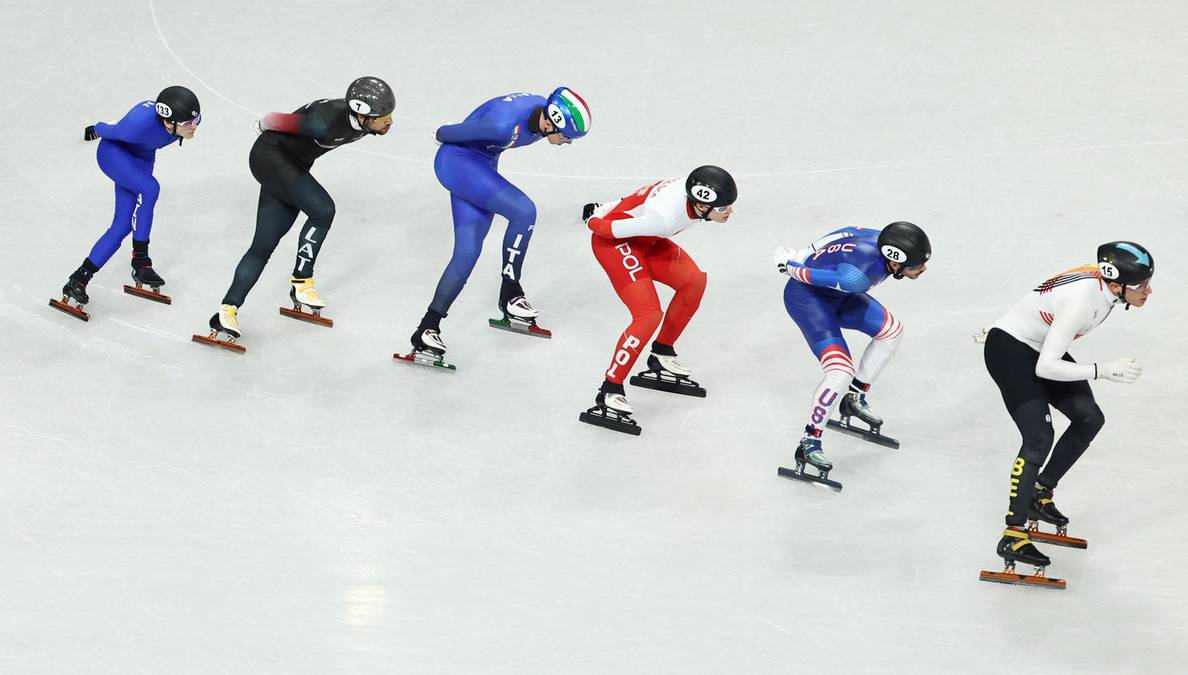 Sześciu zawodnik&oacute;w w kaskach i kolorowych strojach rywalizuje na torze łyżwiarskim.