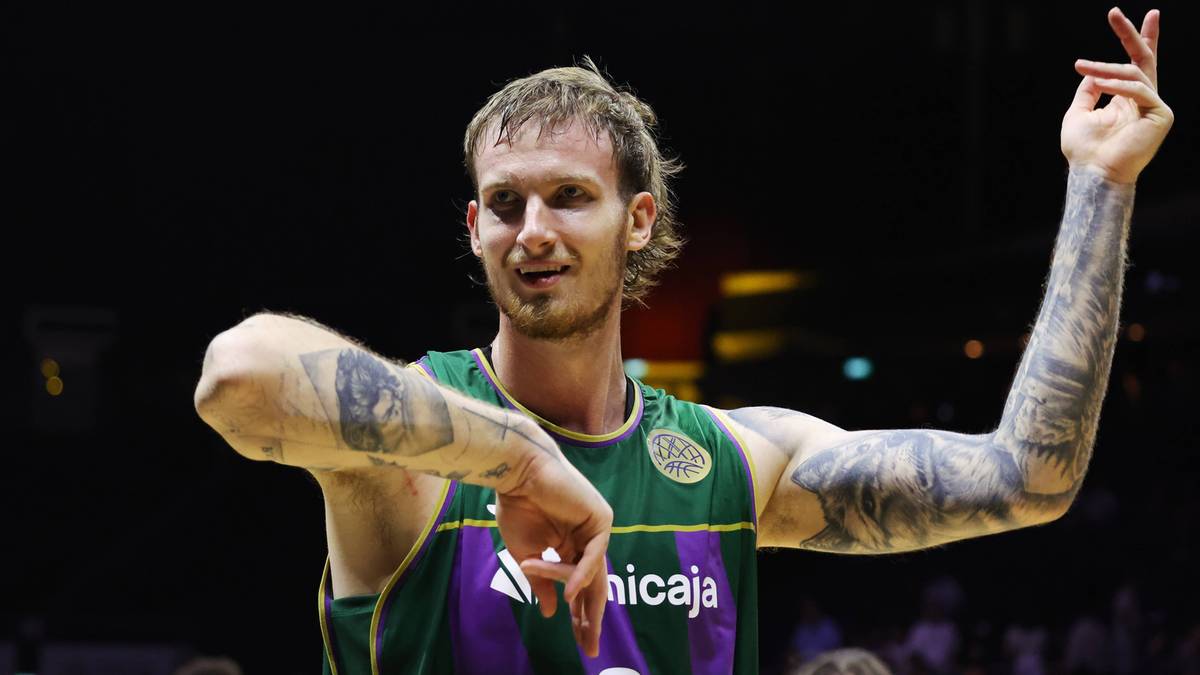 Koszykarz z tatuażami na ramionach w zielono-fioletowym stroju unosi ręce podczas gry.