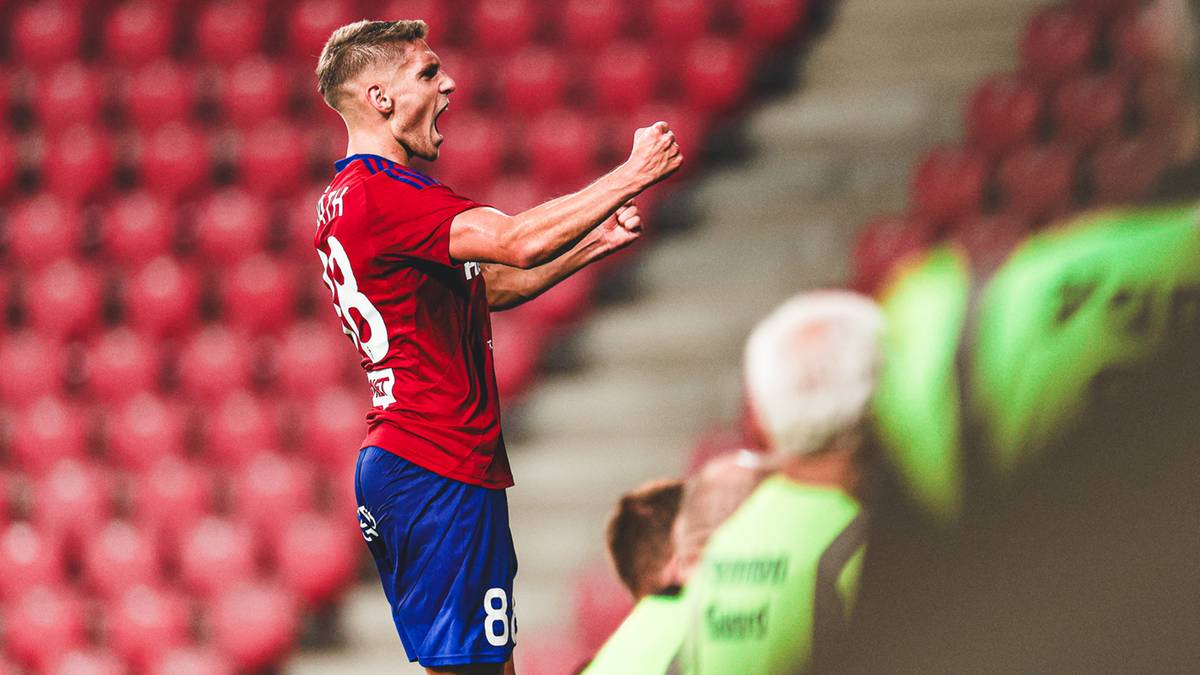 Piłkarz w czerwonej koszulce i niebieskich spodenkach z numerem 8 na plecach cieszy się ze zdobytej bramki na stadionie.