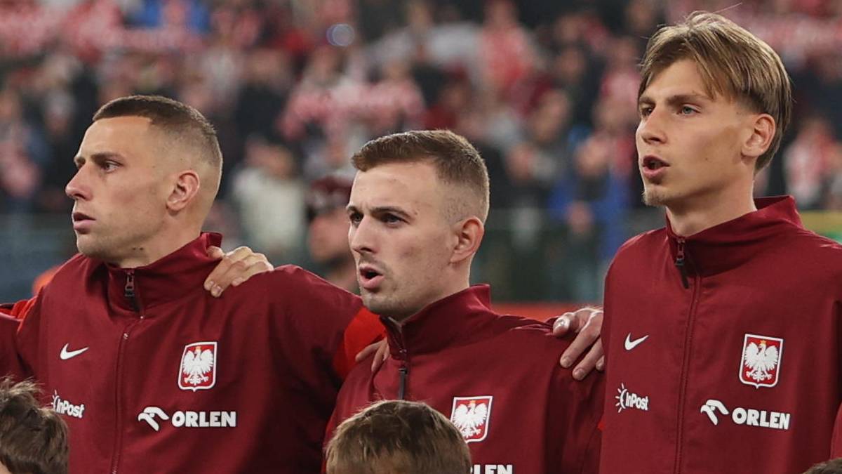 Drużyna piłkarska w strojach biało-czerwonych stoi na murawie stadionu.