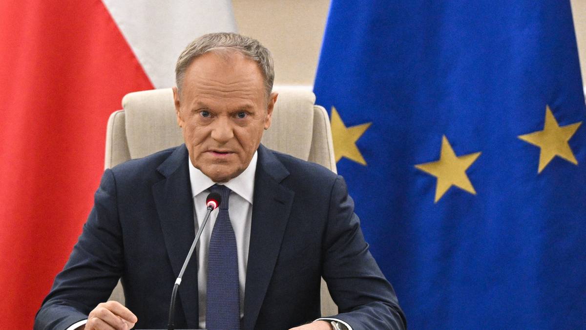 Premier Donald Tusk siedzi przy stole podczas posiedzenia, w tle flagi Polski i Unii Europejskiej.