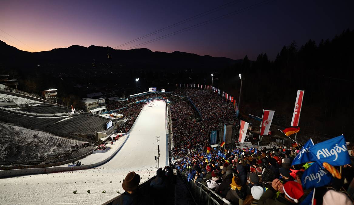 Widok na oświetloną skocznię narciarską nocą, z widownią na trybunach.