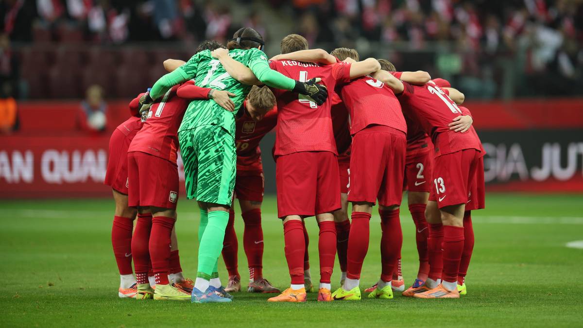 Piłkarze reprezentacji Polski złączeni w kółku na boisku, bramkarz w zielonym stroju pośrodku.