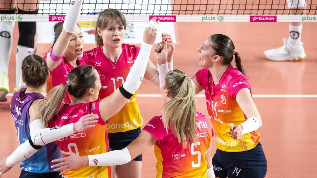 Grupa siatkarek w r&oacute;żowo-pomarańczowych strojach świętuje zwycięstwo na boisku do siatk&oacute;wki.