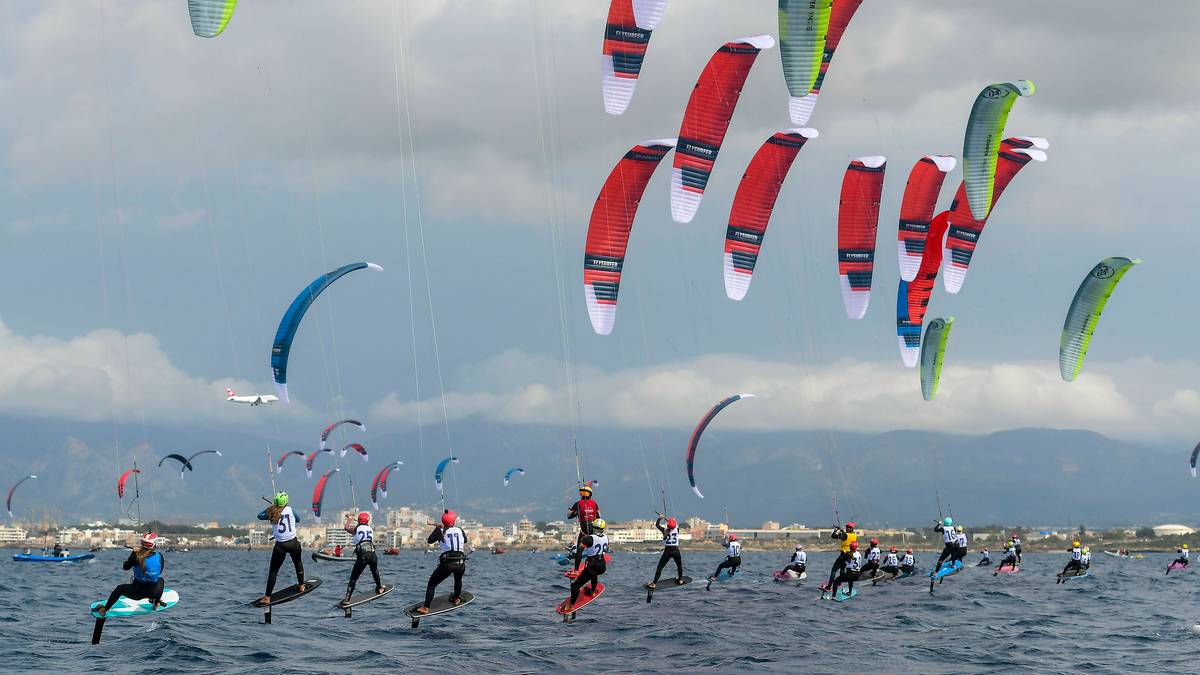 Grupa kitesurfer&oacute;w z kolorowymi żaglami ścigająca się na wodzie.