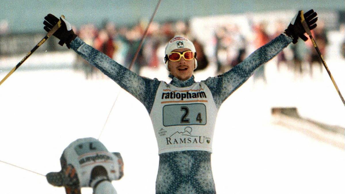 Narciarz biegowy unosi ręce w geście zwycięstwa.