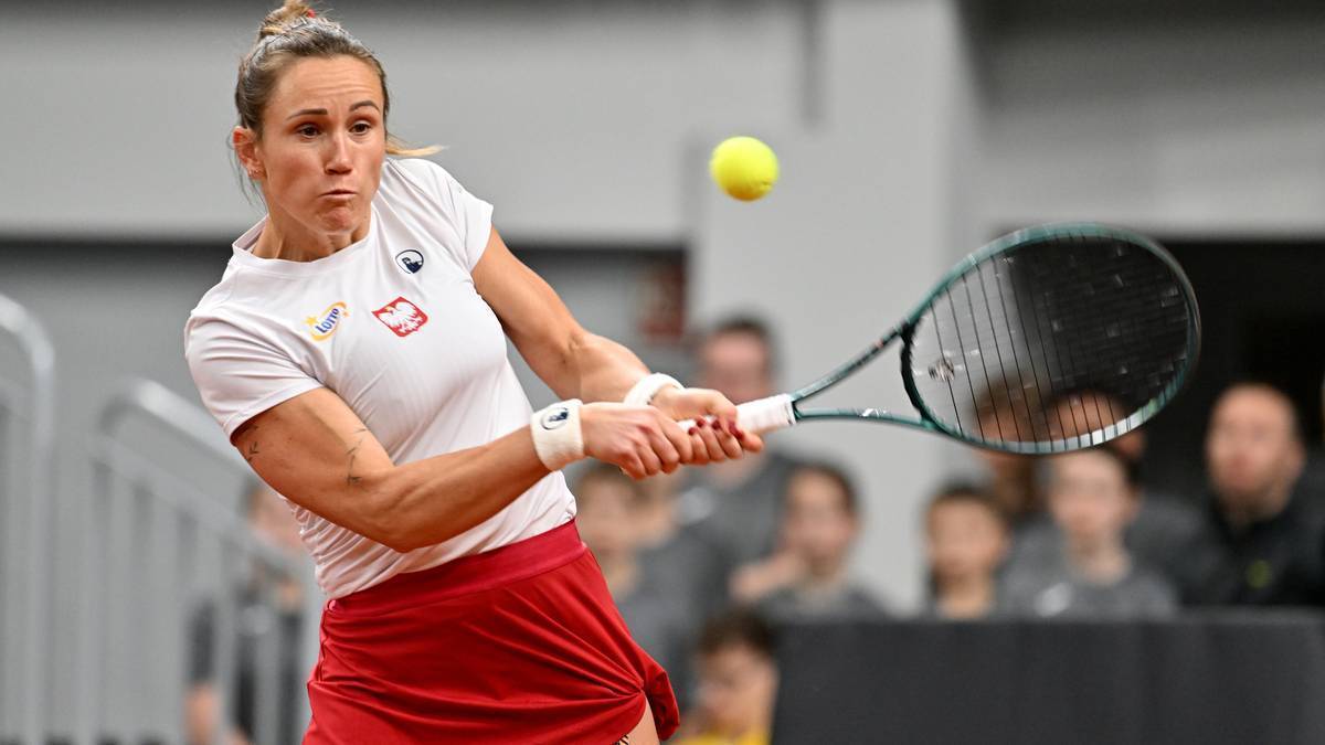 Kobieta w białej koszulce i czerwonej sp&oacute;dniczce uderza piłkę tenisową rakietą.