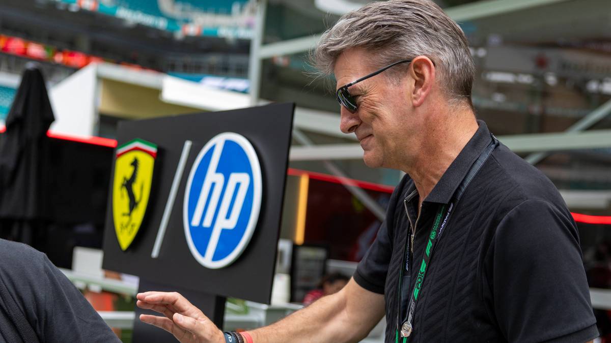 Szef zespołu w okularach przeciwsłonecznych stoi obok tablicy z logo Ferrari i HP.