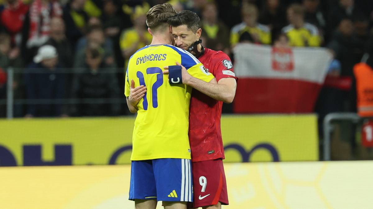 Dw&oacute;ch piłkarzy obejmuje się na boisku, w tle flaga Polski.